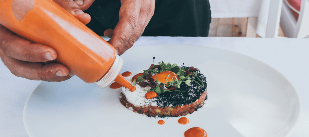 male applying a sauce from a bottle onto a dish